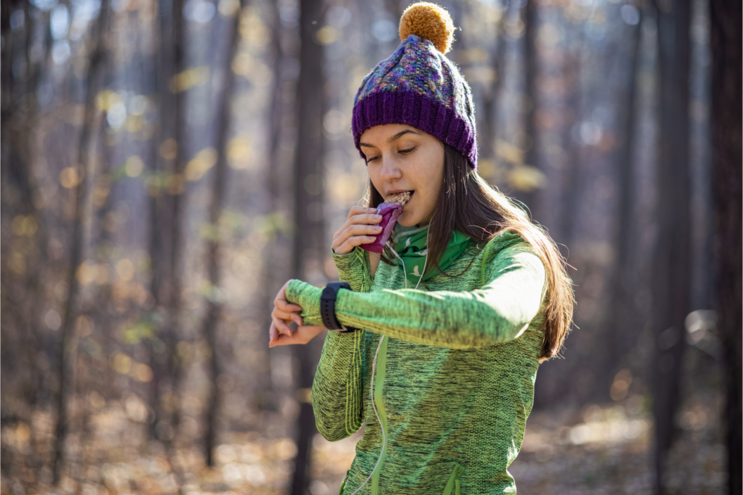 Woman checking her sports wearable while eating a power bar during her run in the forest
